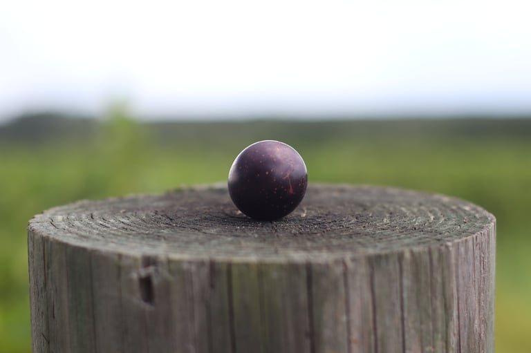 Dark sphere resting on top of a weathered wooden post with green field blurred in background